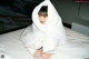 A woman sitting on a bed covered in a white sheet.