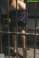 A woman standing behind bars in a jail cell.