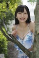 A woman in a blue and white dress leaning against a tree.