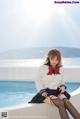 A woman in a school uniform sitting by a swimming pool.