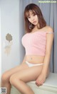 A woman in a pink top and white panties sitting on a dresser.