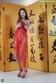 A woman in a red dress standing in front of a yellow wall.