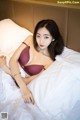 A woman in a red bra laying on a bed.