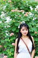 A woman in a white dress standing in front of pink flowers.