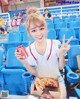 A woman sitting in a stadium holding a pizza and a can of soda.