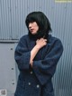 A woman in a blue coat leaning against a metal wall.