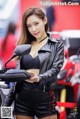 A woman in a black leather jacket and shorts standing next to a motorcycle.