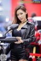 A woman in a black leather jacket and shorts standing next to a motorcycle.