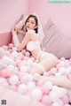 A woman laying on top of a bed covered in pink and white balloons.