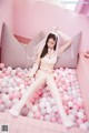 A woman in a white lingerie sitting in a pink ball pit.